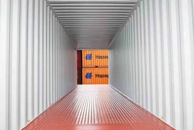 Interior view looking down the length of a clean shipping container, showing the red floor and ribbed walls.