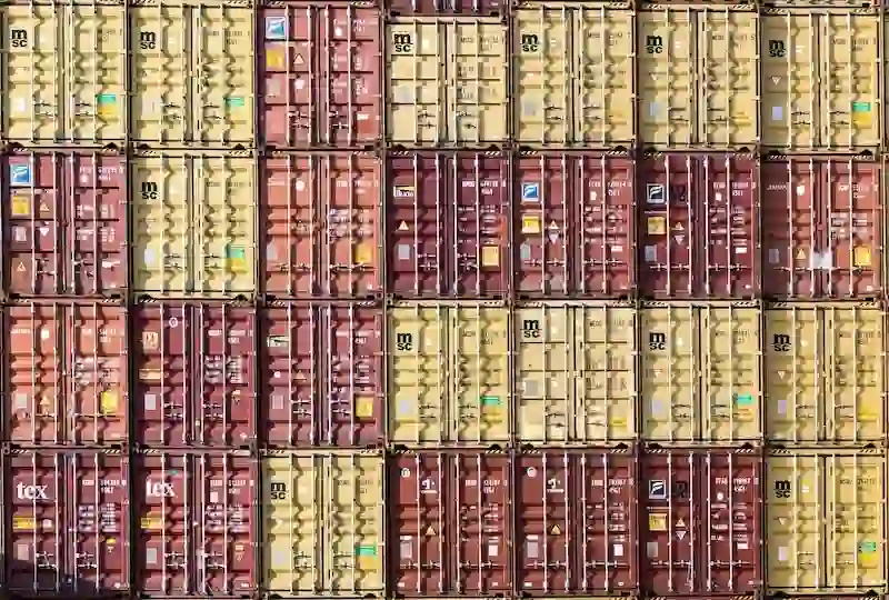 Wall of vertically stacked yellow and red shipping containers, emphasizing the massive weight load and structural engineering.