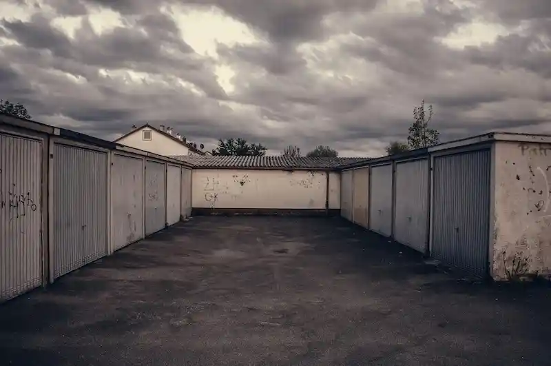Dark, low-angle photo of a row of traditional, run-down garage doors under a cloudy, dramatic sky, symbolizing old storage methods.