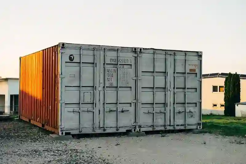 A 20ft shipping container with sunlight hitting the side, showing the door stencils for Tare Weight and Payload.