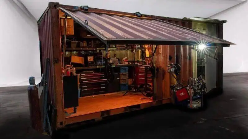 Highly modified rusty container with the side folded down into an awning, revealing a complete welding workshop inside.