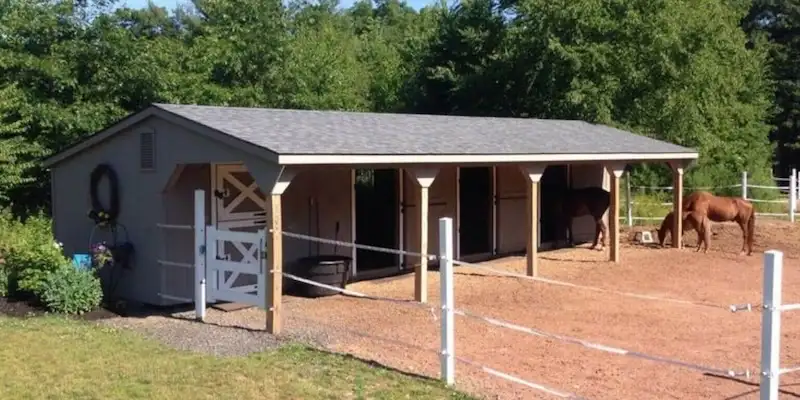Traditional horse barn or run-in shed with asphalt roof and open stalls, used to compare construction costs.