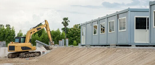 Long row of modular site offices next to an excavator and fresh dirt on a large construction site.
