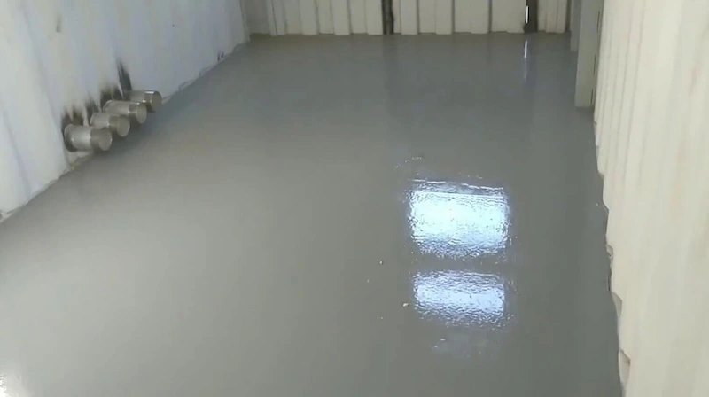 Smooth, glossy gray epoxy floor coating applied inside a shipping container for a clean, seamless finish.