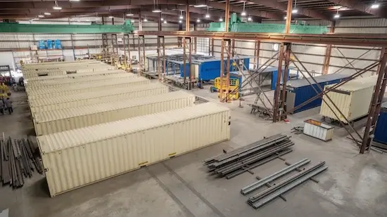 view of a spacious industrial warehouse with rows of beige 40ft shipping containers and raw steel material ready for fabrication or modification.