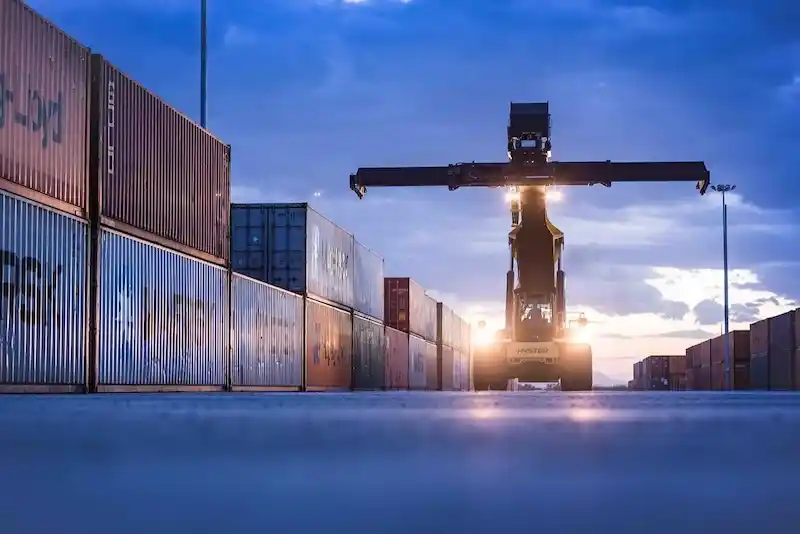 Reach stacker (heavy forklift) operating at dawn in a container yard, symbolizing the specialized equipment needed for massive weights.