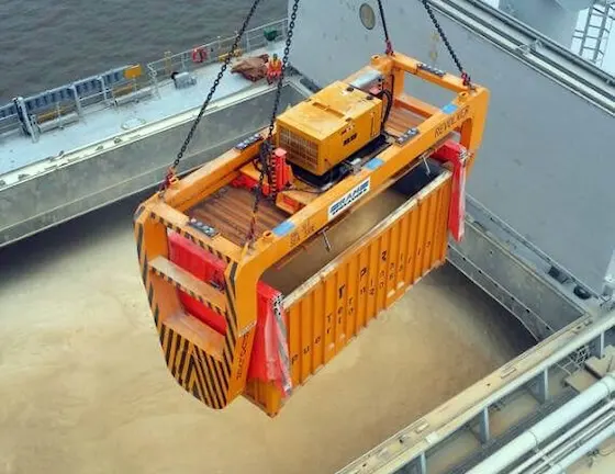 Specialized equipment lifting an open-top container loaded with bulk agricultural cargo like grain from a ship's hold.