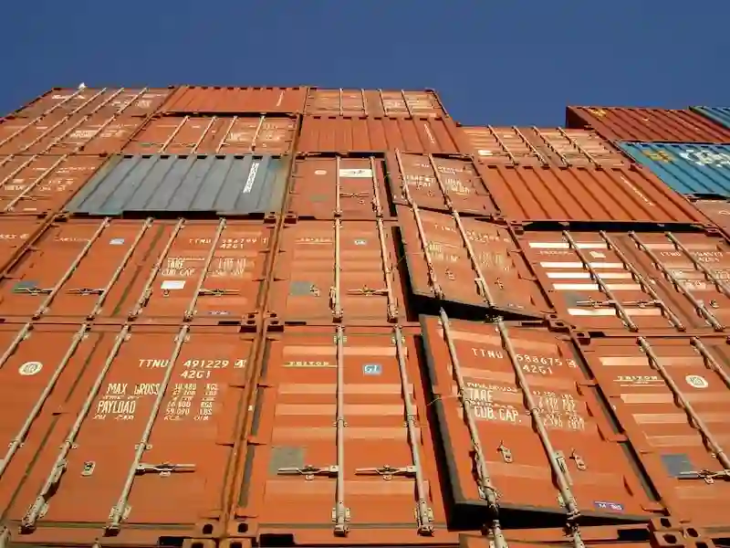 Extreme low-angle view of rust-colored shipping containers stacked very high, showing doors, locks, and weight codes.