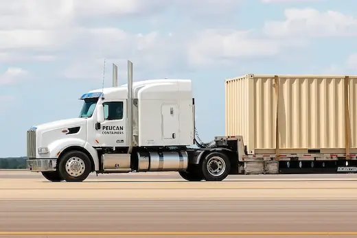 Close-up of a white Pelican Containers semi-truck hauling a single beige 40ft shipping container on a flatbed trailer.