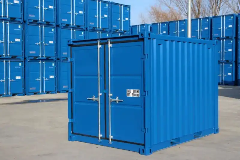 Clean, blue mini container in the foreground, showing tare weight specs, against stacks of full-size shipping containers.