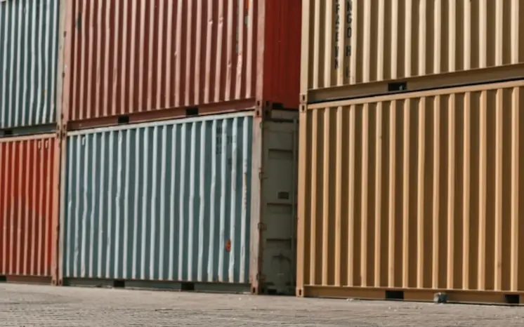A tight, low-angle shot of stacked red, blue, and beige shipping containers in a yard, illustrating the varying colors and cosmetic conditions of our inventory.