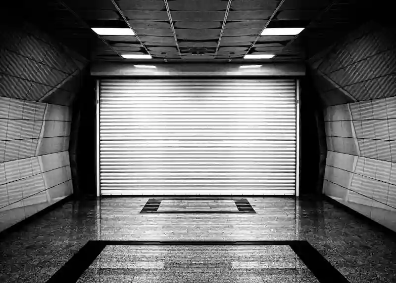 Black and white photo of a sterile, futuristic tunnel ending in a large, sealed metal roller door, symbolizing a secure bunker.