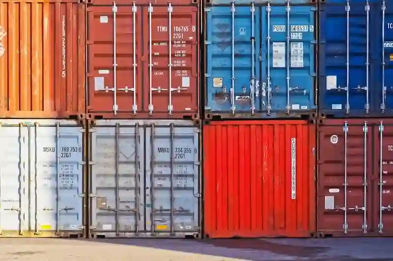 Stacked multi-colored shipping containers showing the end doors, structural rods, and essential size/weight codes.