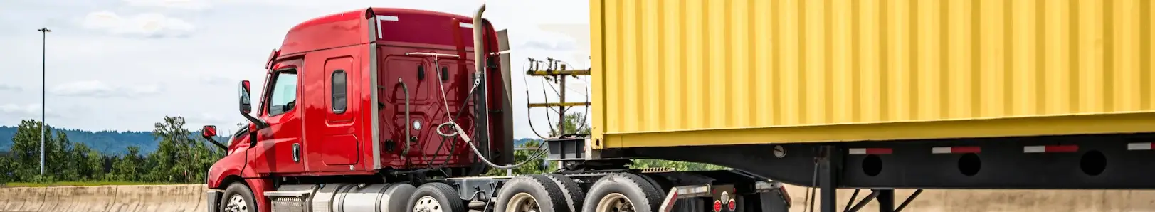 A powerful red semi-truck pulling a flatbed trailer loaded with a bright yellow 40ft shipping container on a major highway, symbolizing long-distance delivery.